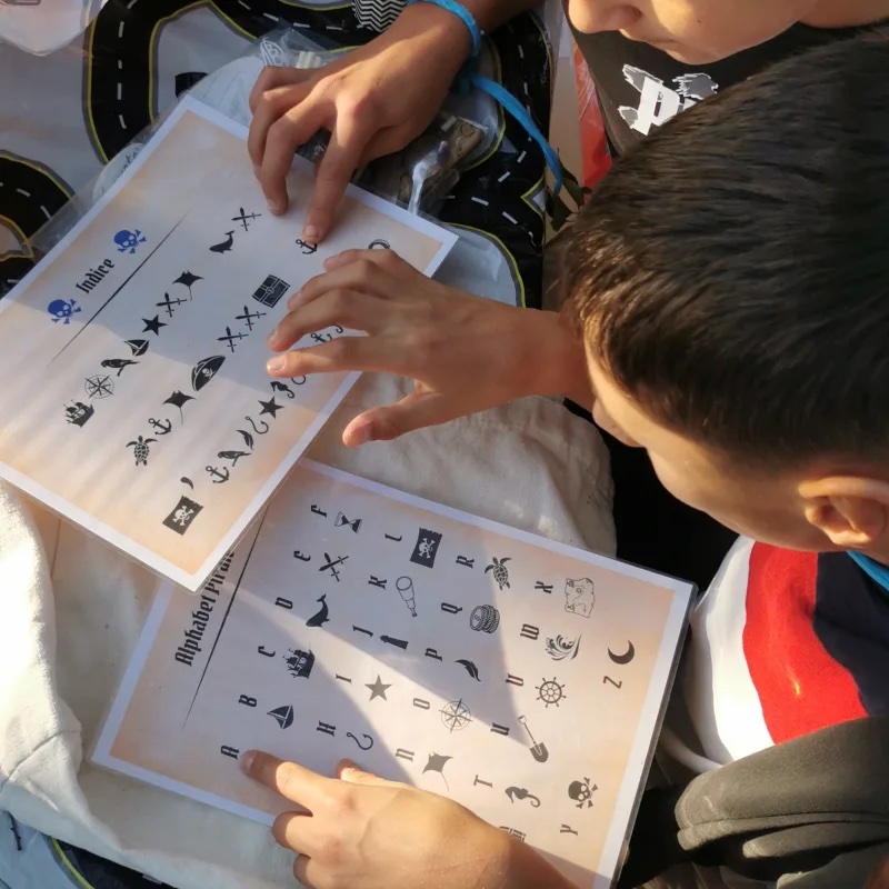 Enfants penchés sur des feuilles décodeur à alphabet pirate, doigts pointés sur les symboles d'une chasse au trésor