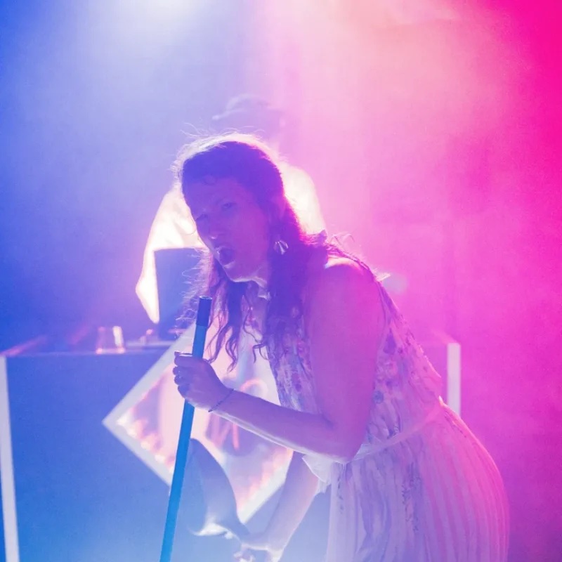 Chanteuse au micro en plein spectacle sur scène, baignée de lumières roses et violettes lors d'un événement animé par Totem